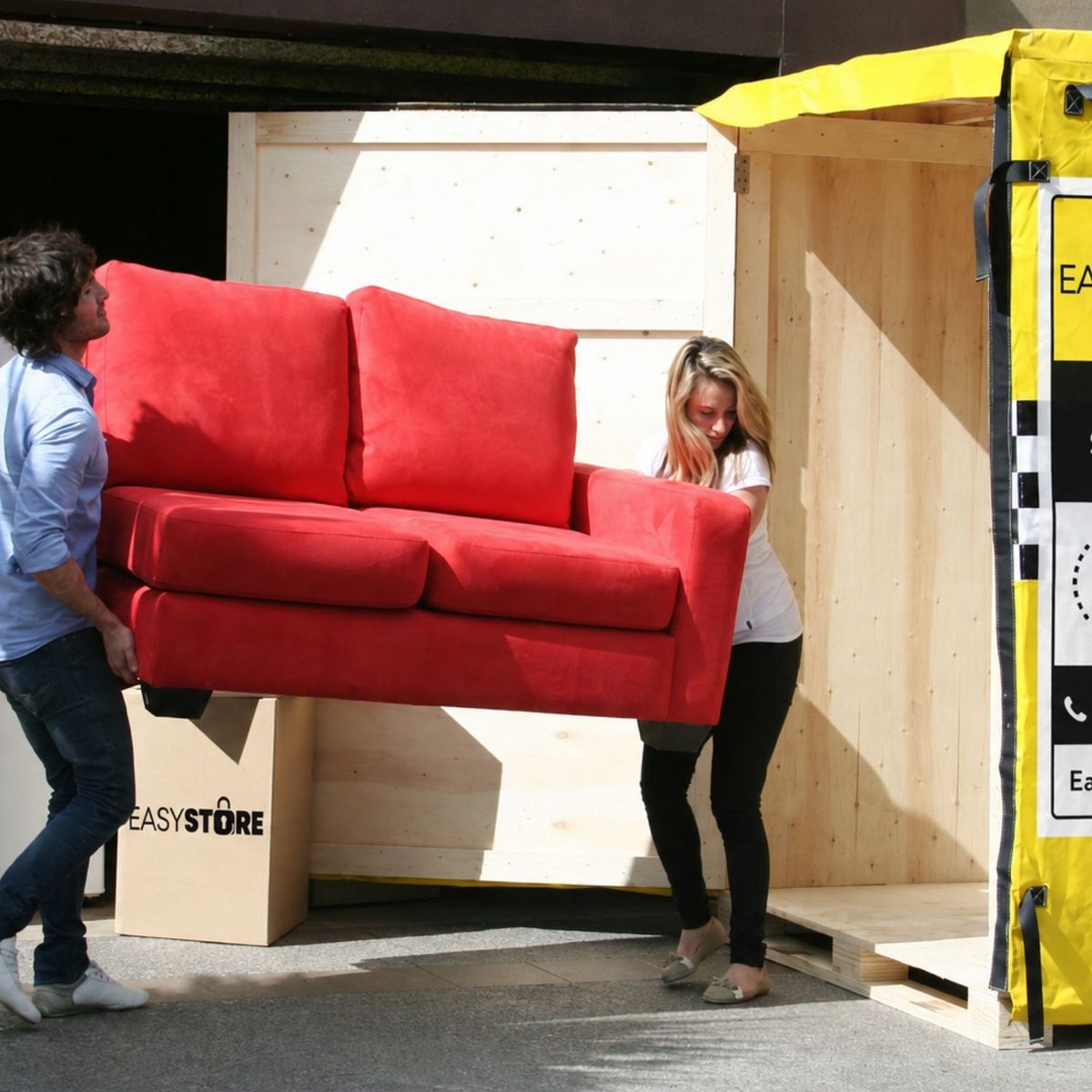 Two people carrying a sofa into an EasyStore storage box at ground level
